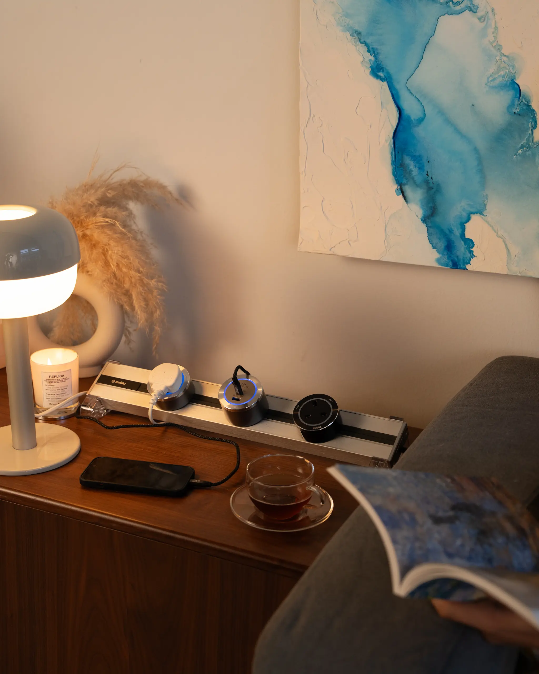 Eubiq track and adapter by a bedside, conveniently charging a phone and powering a lamp for reading.
