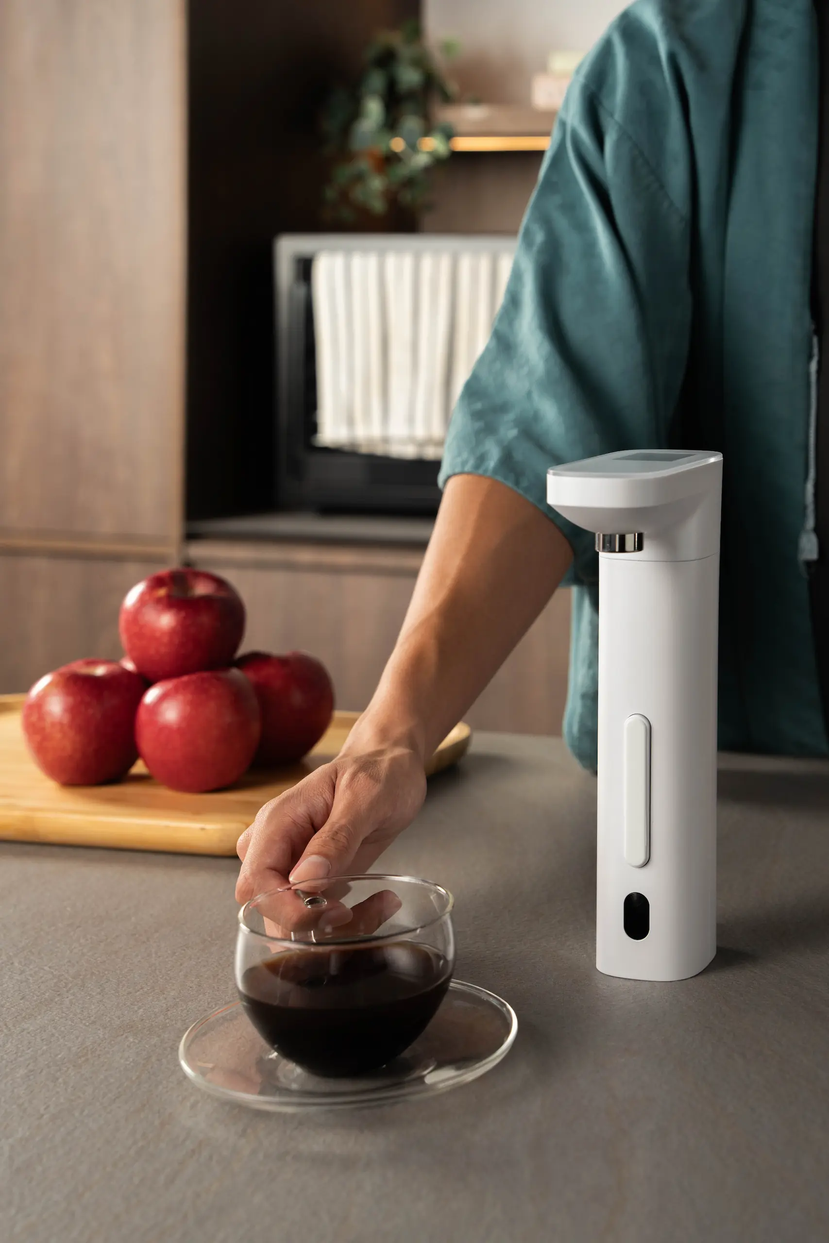 Happie dispenser in a kitchen setting during a morning routine, with fruits on the counter and a hand reaching for a coffee cup, highlighting the dispenser’s role in starting the day.